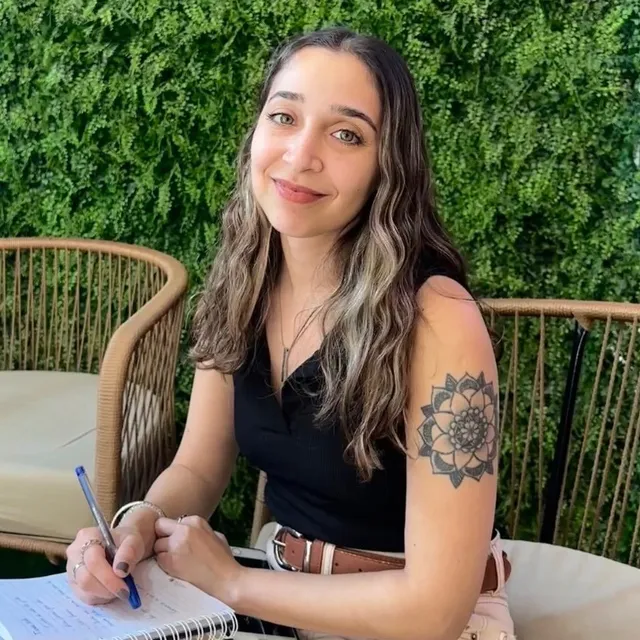 Agustina Siri sonriendo mientras escribe en un cuaderno, frente a un jardín vertical